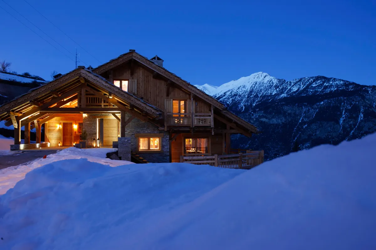 Le Chalet MAJ à la tombée de la nuit, fenêtres éclairées, sous la neige face aux sommets de la vallée de Briançon